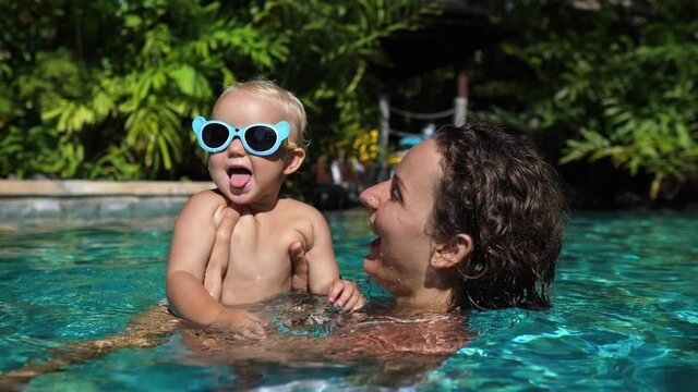 Happy childhood concept. Young Caucasian mom plays with her cheerful baby in the swimming pool 