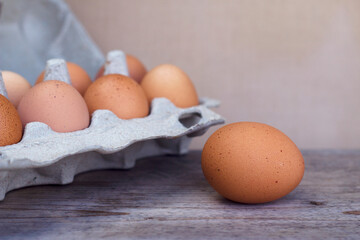 Brown fresh eggs in carton box and one more on the grey wooden table. Organic ingredients for cooking on the kitchen desk close up. Still life food.