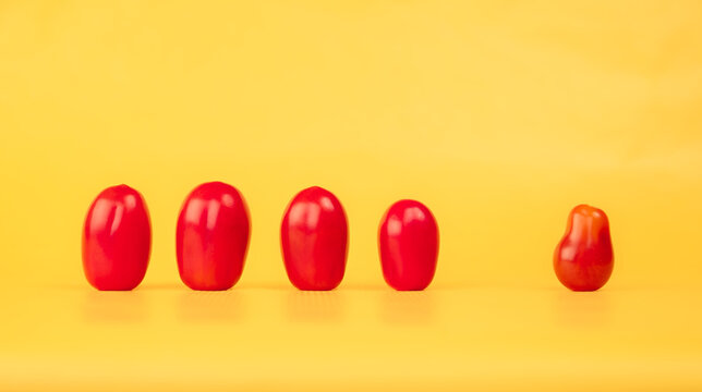 Photo of cherry tomatoes, in a yellow background. Four tomatoes with a similar shape in one side, and a single tomato, with a slightly different shape, on the other side, discriminated.