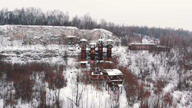 Panoramic footage of Liban Quarry - A historic site where prisoners were kept during Second World War. Old machines and piping equipment. Light snow-fall. Grove of trees in the foreground. 