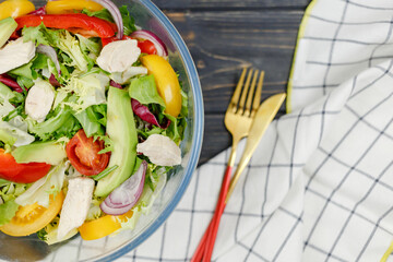 Fresh green salad with avocado, tomatoes, pepper, onion in big white bowl on wooden tray. Vegan salad with green mix leaves and vegetables. Top view on gray table. Healthy vegetarian food. Close up