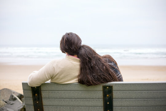 Young biracial couple sitting together on bench by the ocean