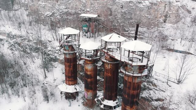 Aerial footage of Old machines and piping equipment in Liban Quarry - A historic site where prisoners were kept during Second World War. Light snow-fall. Snow-covered trees in the background. 
