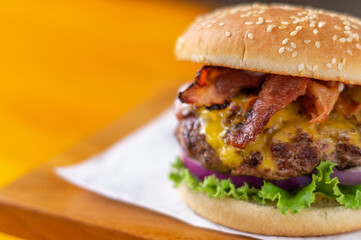 Hamburger with bacon and yellow cheese and fresh vegetables close up