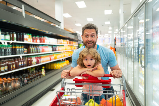 Happy smiling father and child son with shopping cart buying food at grocery store or supermarket.