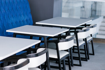 Black and white chairs and tables on a food court against a blue wall. Cafe interior. High quality photo