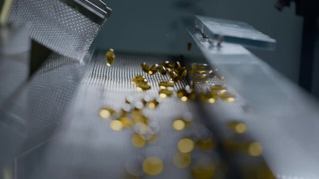 Gelatin capsules in the production of vitamins and medicines. Supplements are made on an automatic medical conveyor equipment. Pharmacological plant of medicines of yellow color. Slow motion