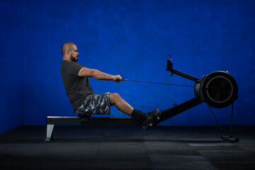Atleta remando en una remadora estática dentro de un gimnasio, con fondo azul © Edgar1 BJ