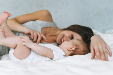 Young mother having fun with cute baby girl on bed with white linen natural tones, love emotion