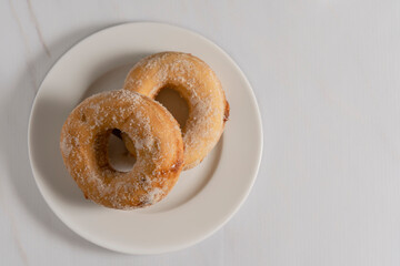 Overhead view of a pair of fudge-filled sugar donuts on a white plate with a white cup. Copy space.
