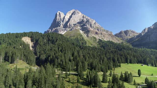 Aerial pullback from massive mountain in the Alps. Flying away from Peitlerkofel over treetops and fields