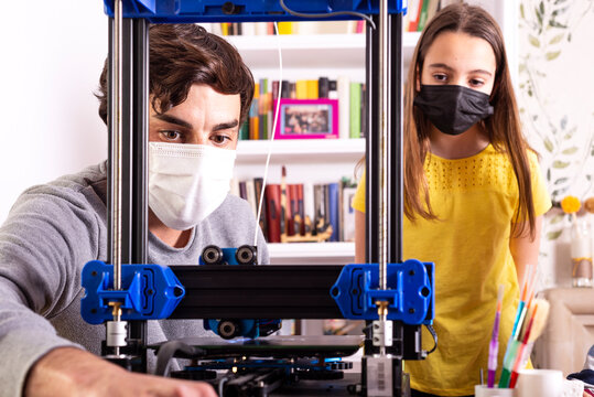 Teacher using a 3D printer with a girl in engineering class. Both wearing face protection mask by covid19.