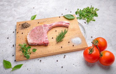 Fresh raw pork with spices and rosemary, oregano and black pepper on wooden slate, on white marble background, pork chop on a bone.