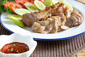 Grilled pork in white dish and chili sauce in cup on  dark brown napery, and brown mat