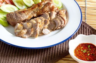 Grilled pork in white dish and chili sauce in cup on  dark brown napery, and brown mat