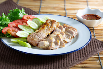 Grilled pork in white dish and chili sauce in cup on  dark brown napery, and brown mat