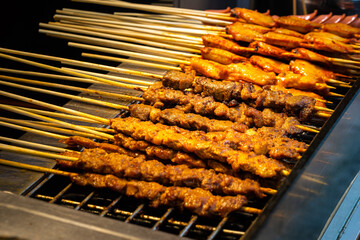 BBQ grilling meat stick on the charcoal oven, topping with spicy pepper powder, Street local food photo. Selective focus at center part of photo.