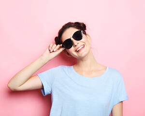 Happy time. Young cute smiling brunette woman wearing casual blue shirt and sunglasses posing over pink background.