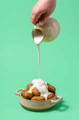 Pouring sour cream over roasted potatoes, minimalist on a green background.