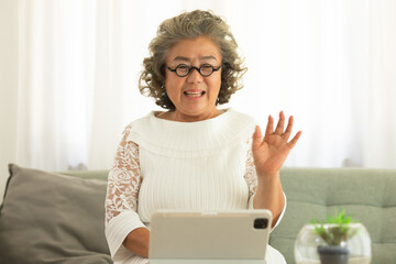 Elderly Asian woman video conferent online with teblet at home.