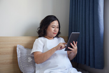 Young Asian Pregnant Woman using digital tablet to search for information 