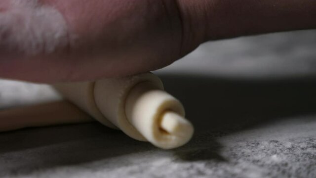 Workers hand twisting up a dought sheet to make a croissant at a bakery plant