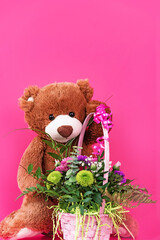 Teddy bear holding blank card and small bouquet on pink