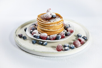 Pfannkuchen mit Himbeeren und Blaubeeren auf einem weißen Teller. Mit Puderzucker bestäubt.  Weiße Hintegrund.