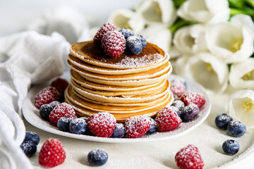 Pfannkuchen mit Himbeeren und Blaubeeren auf einem weißen Teller. Mit Puderzucker bestäubt.  Weiße Hintegrund.