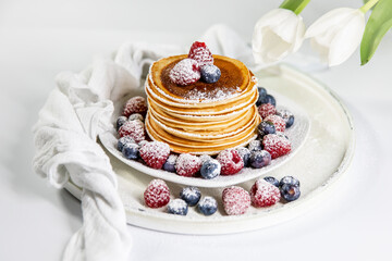 Pfannkuchen mit Himbeeren und Blaubeeren auf einem weißen Teller. Mit Puderzucker bestäubt.  Weiße Hintegrund.