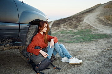 woman tourist in the mountains on nature sits near the car and mountains road landscape