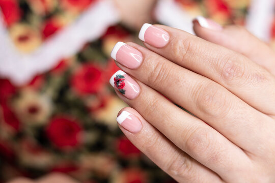 Manicure. White French jacket and red flower design gel paints on the nails of a young girl. Nail care in a beauty salon. Close-up