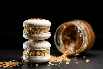 Macarons mit Karamellchips auf einem schwarzen Hintergrund. Im Hintergrund ein umgestürztes Glas...