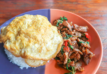 Fried basil leaves with beef and omelette on rice Thai food on wood background