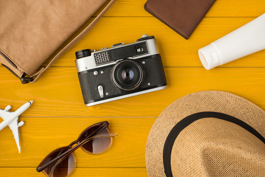 Above photo of sunhat camera bag sunglasses passport sunblock and airplane isolated on the yellow wooden background