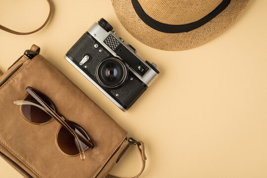 Top view photo of sunhat camera and sunglasses on leather bag on isolated beige background