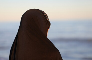arab woman with black dress covering her hair by the sea in summer