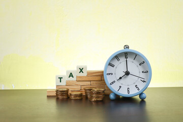 Tax and time concept.  Block letters on Tax on the wooden blocks with stacked coins and alarm clock
