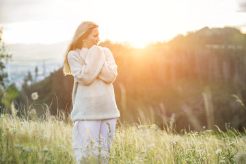 Fototapeta na wymiar Happy woman enjoying sunset stay on the green grass on the forest peak of mountain. Fresh air, Travel, Summer, Holidays. Health care, authenticity, sense of balance and calmness.