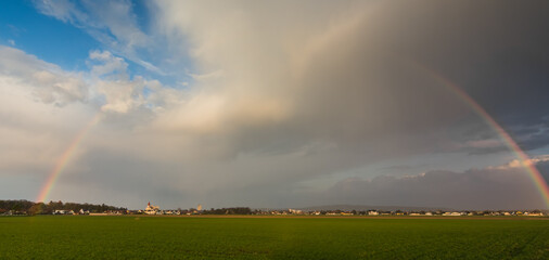 Obraz na płótnie Canvas wonderful large rainbow with a village green field and wonderful sky panorama