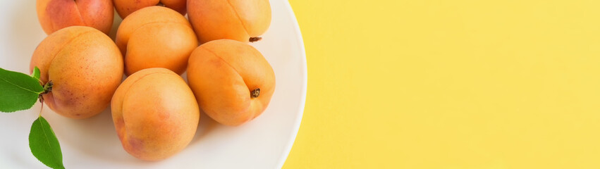 Pile of apricots in a white plate on yellow background with copy space banner