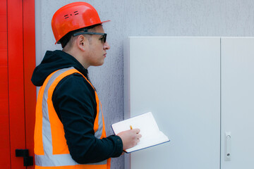 Electrical engineer inspects the switchboard, writing down the faults in a notebook. Maintenance of...