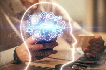 Double exposure of man's hand holding and using a digital device and brain hologram drawing. Data concept.