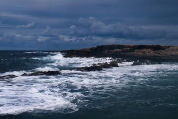 Fototapeta premium White foam and waves in the blue ocean at a rocky beach in Qawra, Malta on a stormy day.