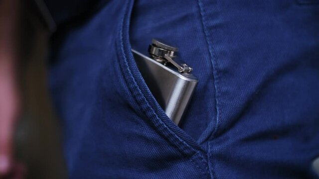 Caucasian Drinking Man Pulling Out and Putting In Shiny Metal Hip Flask of Whisky Alcohol Concealed in Trousers Pocket