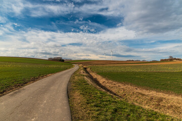 Rural landscape with road, fields, meadows, small forest, wind farm and blue sky with clouds