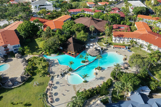 Aerial Shot Of A Pool In A Resort Area Surrounded By Greenery And Buildings Under The Sunlight