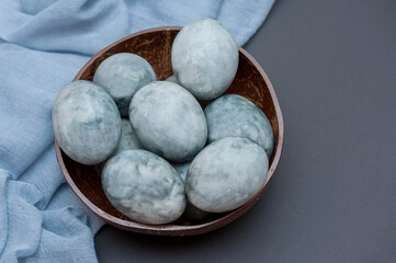 Marble Easter eggs on a dark background, lie in a wooden coconut cup on a black background. The...