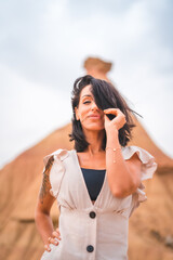 Fototapeta premium Sensual gazes from a brunette Caucasian girl in an explorer outfit with a white dress in a desert on a cloudy afternoon