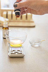 A soap-maker woman weighs aromatic oils for making cosmetics on a kitchen scale. Home spa. Small business